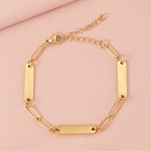 Close-up of three gold-tone rectangular metal plates on a paperclip chain bracelet