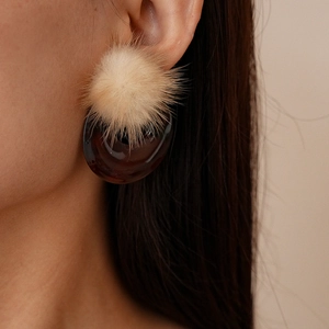 Detail of C-shaped resin earring with tortoiseshell texture and beige faux fur ball