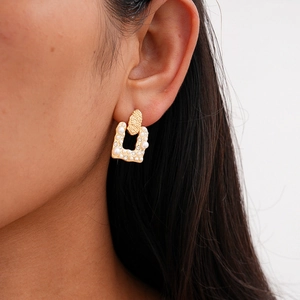Detailed close-up of a U-shaped gold earring with pearls and rhinestones on a model