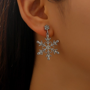 Detailed view of silver snowflake earring with sparkling rhinestones worn on ear.