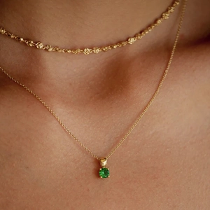 Close-up of layered gold S925 silver necklaces featuring a round green birthstone pendant