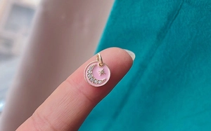 Macro shot of a pink enamel round pendant with a sparkling moon and gold star
