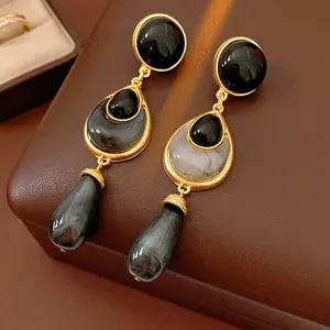 Vintage floral teardrop earrings in gold with dark stones on a brown leather box