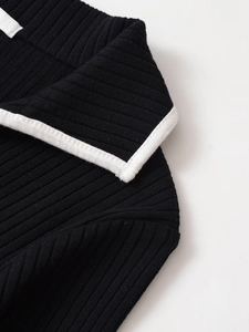 Dettaglio dello scollo a V con profilo bianco a contrasto su maglia a coste nera