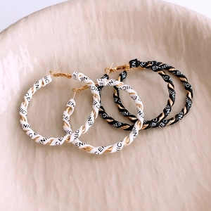 Macro detail of leather wrapped gold hoops with embossed letters in black and white