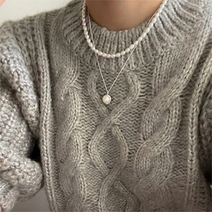 Close-up of layered 925 silver necklace with white pearls on a grey knit sweater