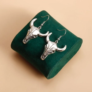 Détail de boucles d'oreilles crâne de bœuf argentées au style punk vintage sur velours