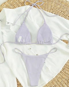 Flat lay of light purple ribbed bikini set with halter ties on a woven mat