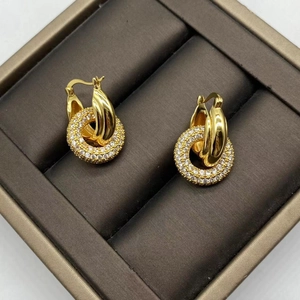 Macro shot of interlocking gold metal ring and sparkling zircon-studded earring detail