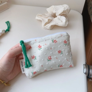 Close-up of floral cotton pouch with green cord zipper pull and simple wish side label