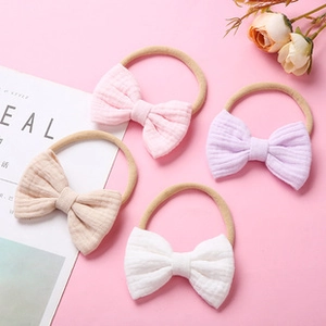 Flat lay of 4 soft cotton gauze baby bow headbands in pink, lilac, beige and white colors