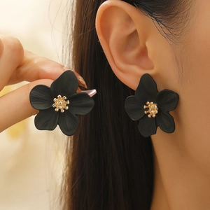 Gros plan détaillé de boucles d'oreilles fleurs noires et pistils dorés sur modèle