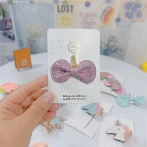 Close-up of pink glitter bow hair clip with golden unicorn horn on a display card