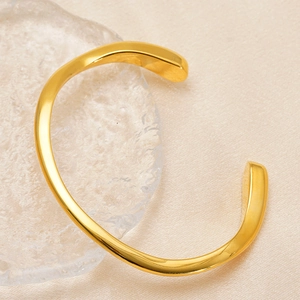 Dettaglio ravvicinato del bracciale rigido dorato in acciaio su tessuto di seta