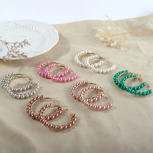 Detailed flat lay of beaded hoop earrings in six colors on beige textured fabric
