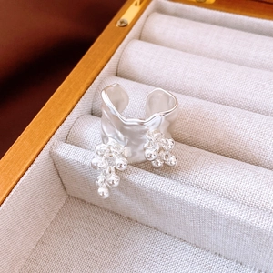 Detailed macro view of silver irregular fold ring with metal bead tassel on beige tray