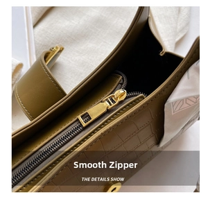 Detail of smooth gold zipper and crocodile embossed texture on olive green baguette bag