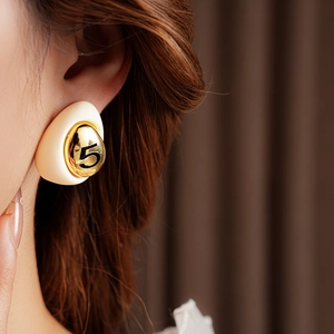 Detail of drop-shaped gold-plated earring with number 5 on cream enamel ball