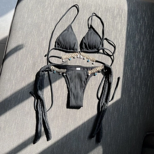 Detail of black pleated bikini featuring gold chains and bohemian charms