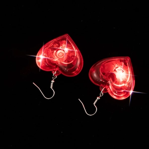Detailed macro view of glowing red LED heart-shaped earrings on a black background.