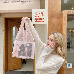 Detail of pink mesh tote bag with 3D floral embroidery shown in a lifestyle street setting