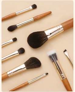 Detail view of 8 mini makeup brushes with wood handles and golden ferrules on beige