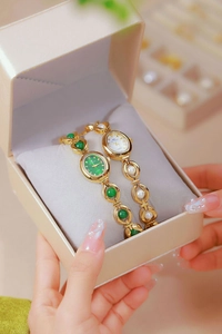 Close-up of gold chain watches with green jade and pearl accents in a gift box