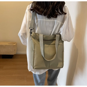 Rear view of model wearing a light green canvas tote bag with shoulder straps for commuting