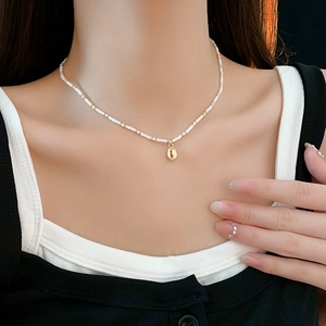 Close-up of Bohemian seashell pendant necklace with white and gold beads on neck