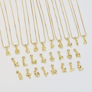 Flat lay of 26 gold plated copper bubble initial pendants on box chains over white backdrop