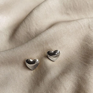Polished silver heart stud earrings resting on elegant champagne silk fabric background