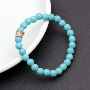 Detail of turquoise beaded bracelet with rose gold crown charm on black and white surface