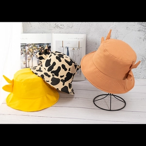 Cute cow print and solid color bucket hats with small horns on a wooden tabletop