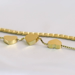 Detail of 18K gold double-layer bracelet featuring heart pendants and a flat snake chain