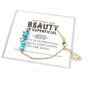 Detail of gold chain bracelet with irregular turquoise stones on a white display card