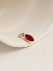 Macro detail of 18K gold plated marquise red zircon pendant on white ceramic tray