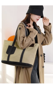 Detail einer khakifarbenen Canvas-Tragetasche mit schwarzen Riemen über einem Trenchcoat