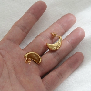 Detailed view of hand holding polished golden stainless steel crescent stud earrings