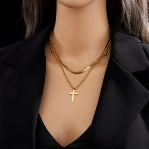 Detail van gelaagde gouden kruisketting met slangen- en kralenkettingen op een blazer