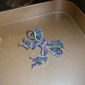 Detail shot of a purple and green bow brooch with zircons on a golden tray