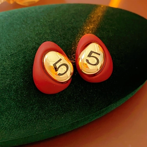 Detailed close-up of vintage gold earrings with red drip oil finish and black number five