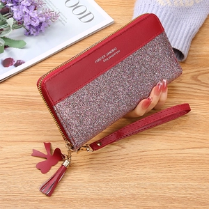 Close-up of a red leather wallet with glitter patchwork, tassel detail, and hand strap