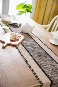 Close-up of woven table runner with beige and black stripes on a wooden dining table