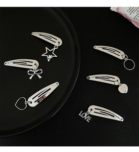 Detail of silver metal hair clips set featuring star, heart, and bow charms on black background
