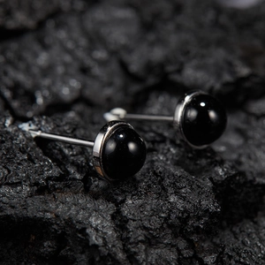 Macro shot of minimalist S925 sterling silver studs with round black stone on dark rock