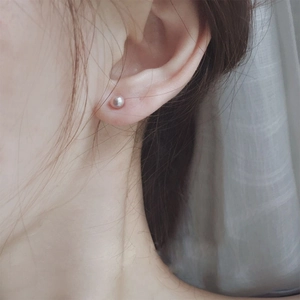 Close-up of a minimalist round pearl stud earring with light pink luster on a model ear