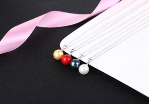 Detailed view of simple silver necklaces with colorful pearl pendants and pink ribbon