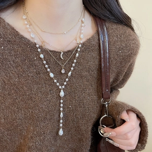 Close-up of layered gold necklace with pearls, moon and star pendants on a brown sweater