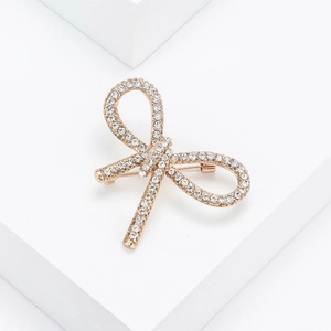 Detailed view of a gold bow brooch with sparkling rhinestones on a white display stand