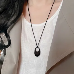 Collier minimaliste à pendentif ovale évidé noir porté par un mannequin en tenue chic